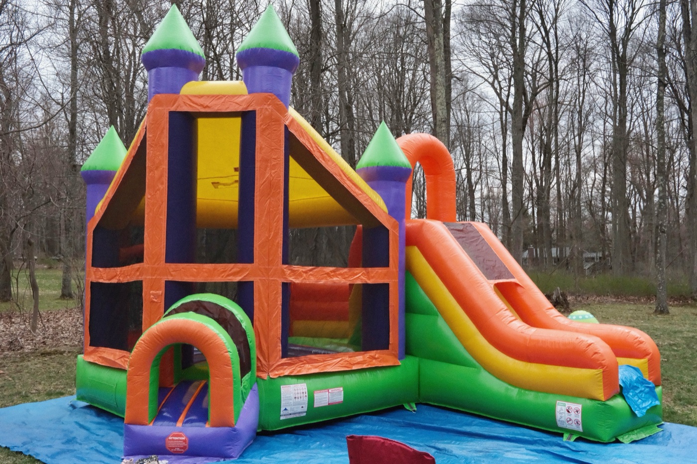 Rainbow inflatable castle bounce and slide combo with purple turrets and mesh windows, product photo on white