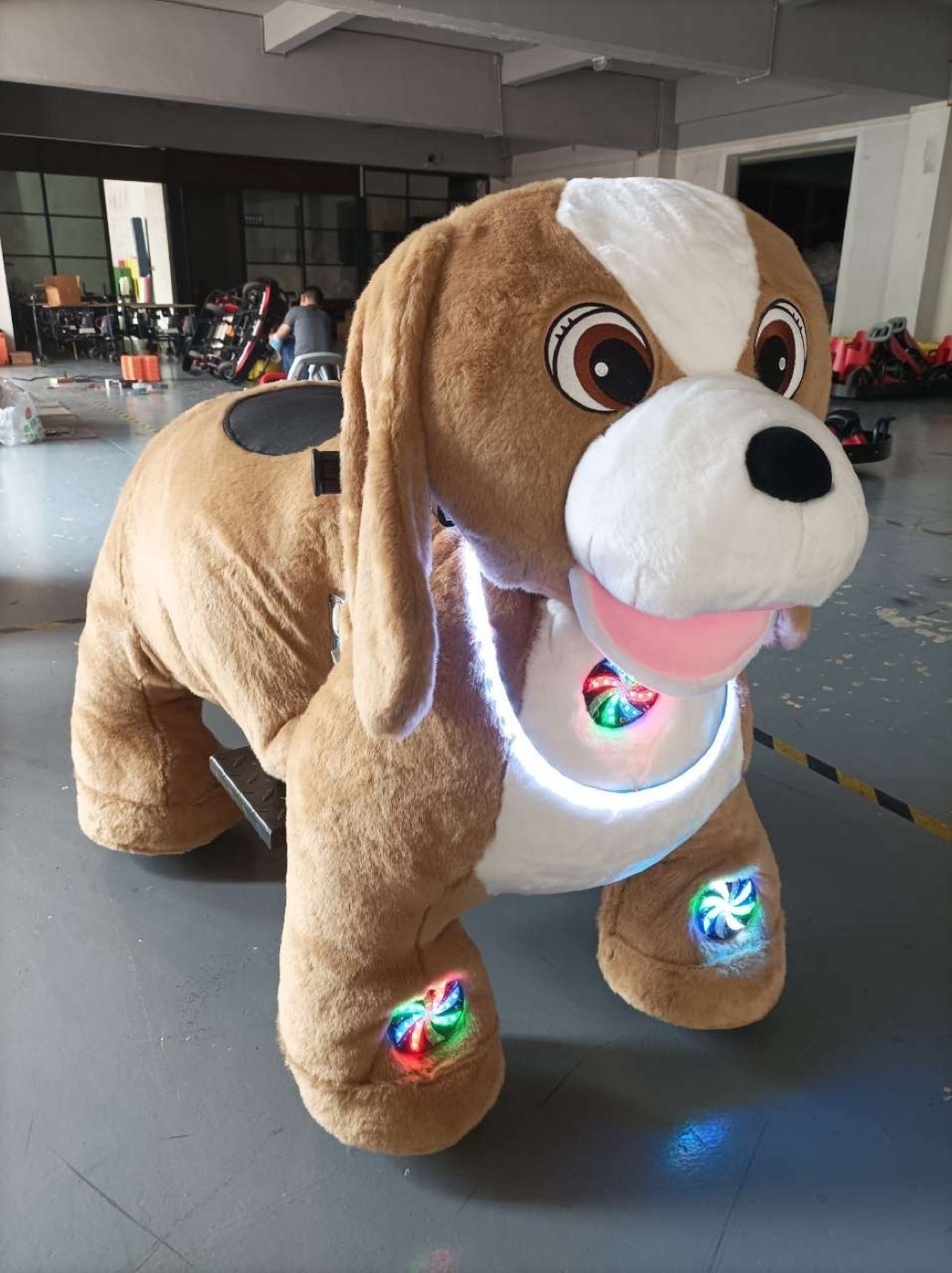 Large tan plush ride-on dog character with LED light accents on the chest and paws, shown indoors